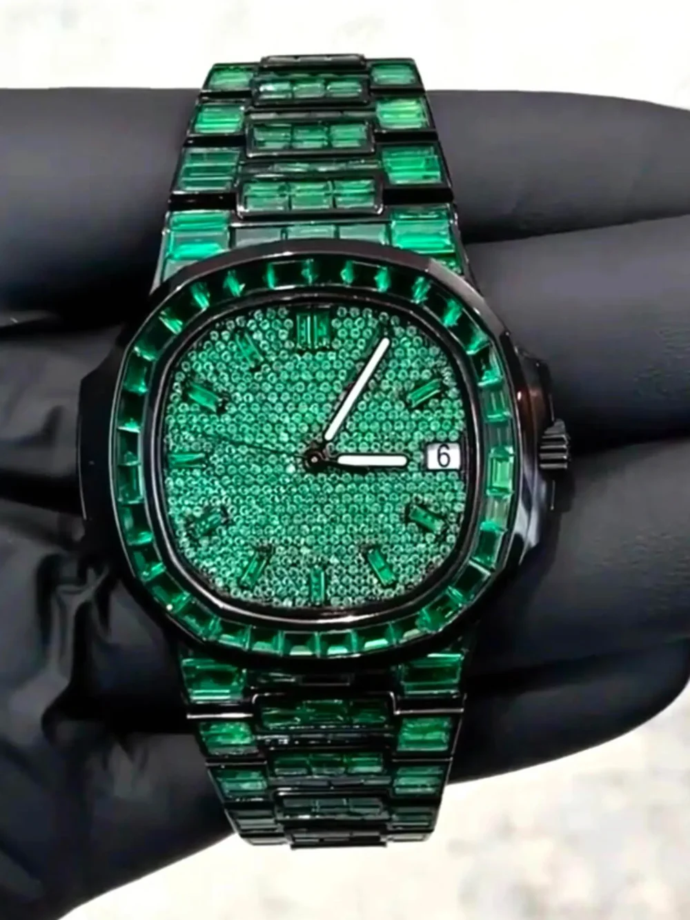 VVS1 Moissanite "Emerald" Flood: Fully handset with D-Color VVS1 Moissanite stones in a rare emerald green shade that passes thermal diamond testers. Baguette-Cut Bezel & Band: Features high-grade baguette-cut stones on the bezel and every link of the band for a clean, architectural shine. Stealth Black PVD Finish: Crafted from 316L stainless steel with a premium black PVD coating for a scratch-resistant, high-end matte-to-gloss look. Micro-Pave Dial: The watch face is fully flooded with round-cut green moissanite stones, offering 360-degree light refraction. Precision Date Function: Includes a functional date window at 3 o'clock, blending tactical utility with high-jewelry aesthetics.