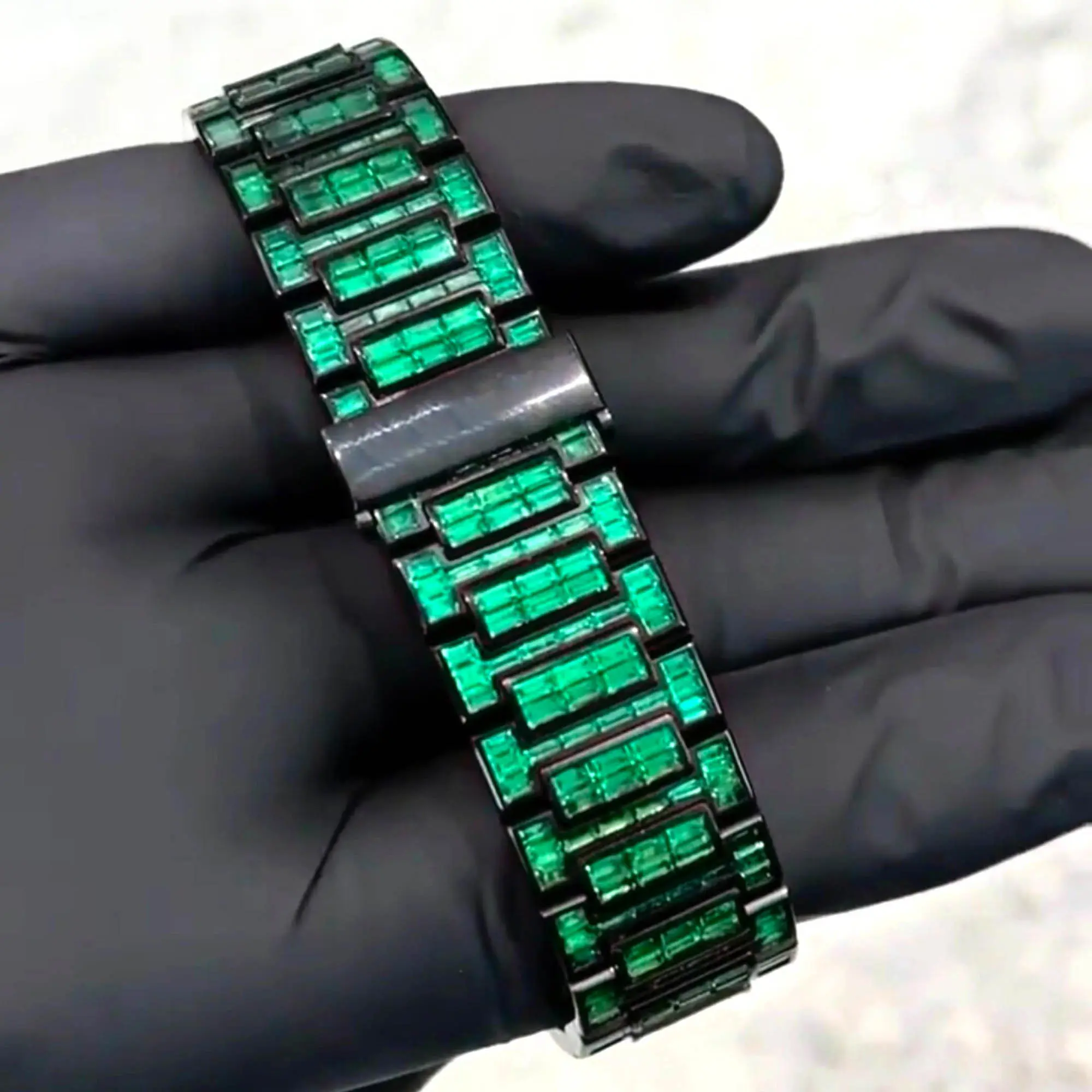 VVS1 Moissanite "Emerald" Flood: Fully handset with D-Color VVS1 Moissanite stones in a rare emerald green shade that passes thermal diamond testers. Baguette-Cut Bezel & Band: Features high-grade baguette-cut stones on the bezel and every link of the band for a clean, architectural shine. Stealth Black PVD Finish: Crafted from 316L stainless steel with a premium black PVD coating for a scratch-resistant, high-end matte-to-gloss look. Micro-Pave Dial: The watch face is fully flooded with round-cut green moissanite stones, offering 360-degree light refraction. Precision Date Function: Includes a functional date window at 3 o'clock, blending tactical utility with high-jewelry aesthetics.